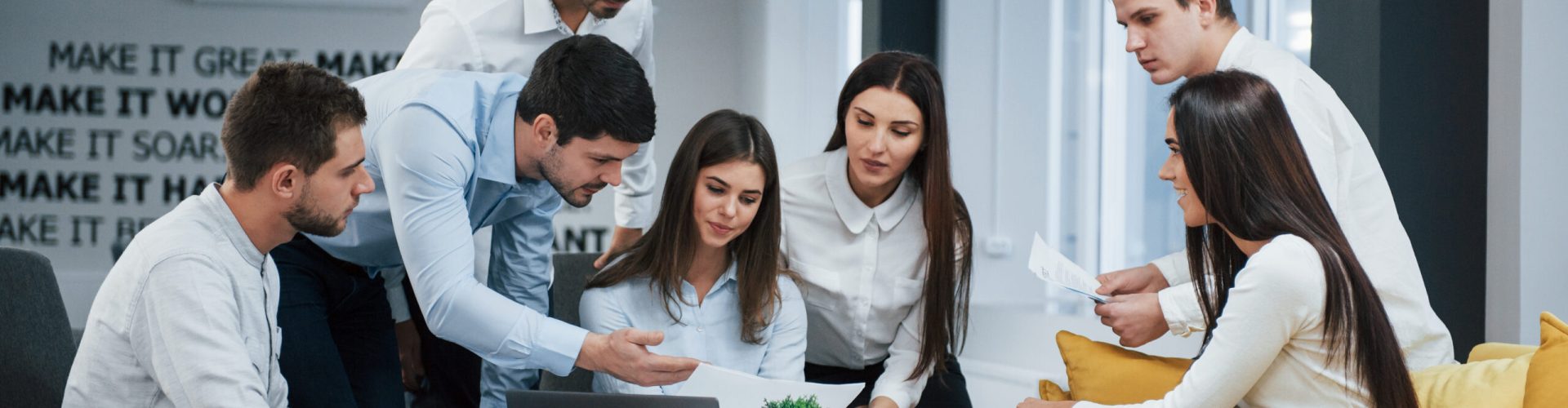 Guy shows document to a girl. Group of young freelancers in the office have conversation and working.